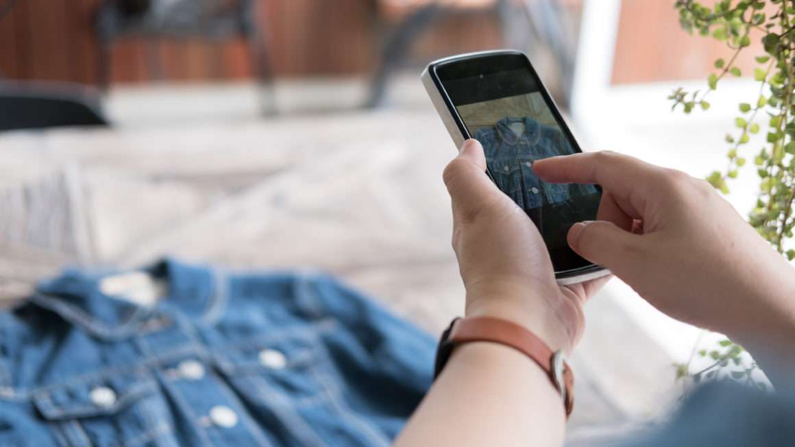 Man selling taking photo of denim jacket on phone to sell online