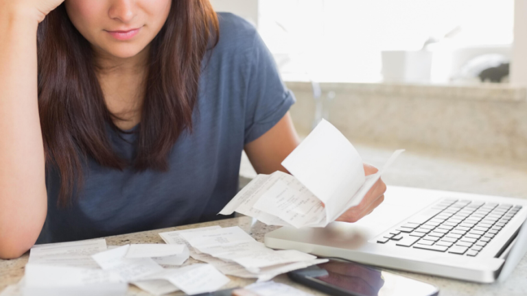 Woman in kitchen looking worried over bills