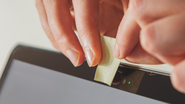 A hand putting sticky tape over laptop webcam