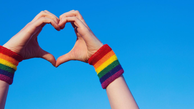 Hand making a heart sign with gay pride LGBT rainbow flag wristband