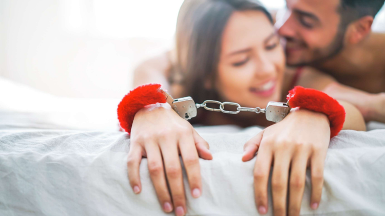 Couple playing sex games in bed with red furry handcuffs