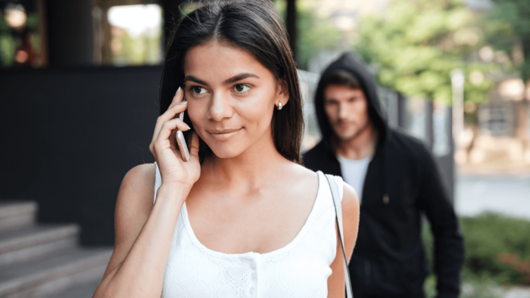 Beautiful young woman talking on mobile phone and being stalked by man criminal on the street