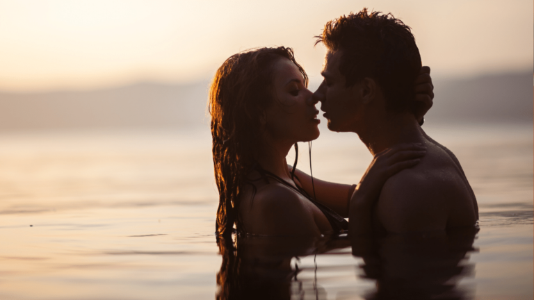 Couple of young lovers kissing in the water at dawn