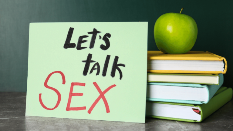Books, apple and sign with phrase "Let's talk sex" on grey table near chalkboard
