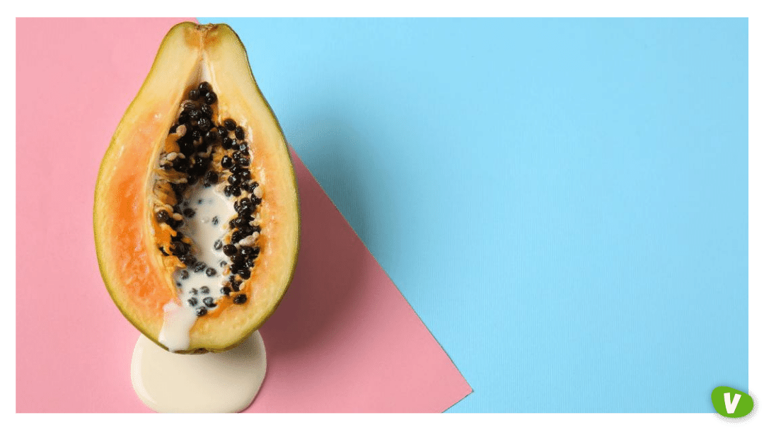 Half of papaya with dripping white liquid on color background