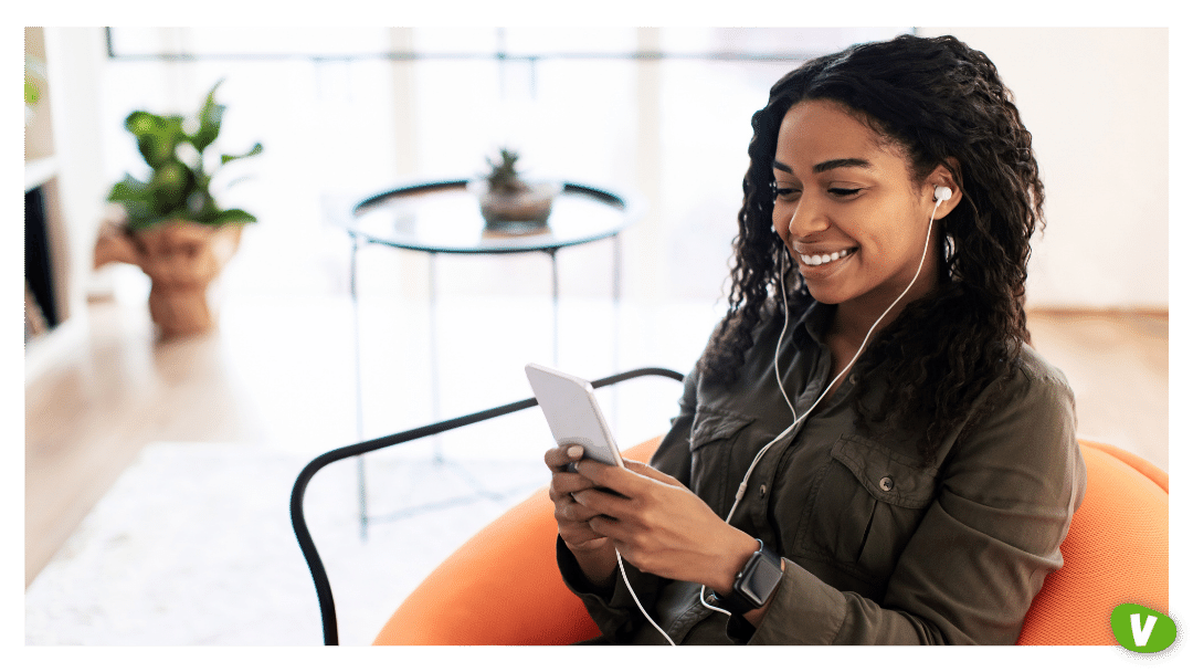 African American woman wearing headphones listening to music or a podcast using smartphone