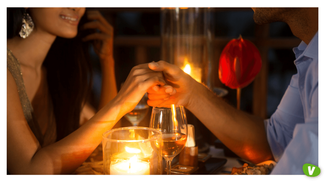couple holding hands together over candlelight during romantic dinner