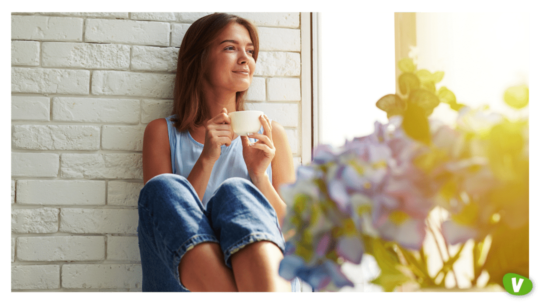 young girl enjoying an ideal day sitting in the window-sill wearing casual denim jeans and loose light-blue blouse, crossing legs and looking through the window