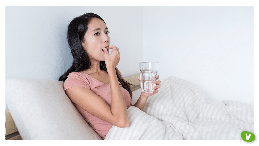 woman in bed taking pills holding a glass of water