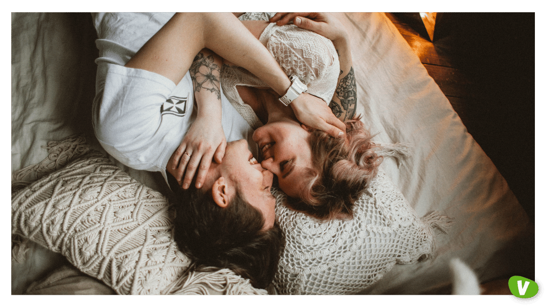 couple in bed lovingly smiling at each other and holding each others faces