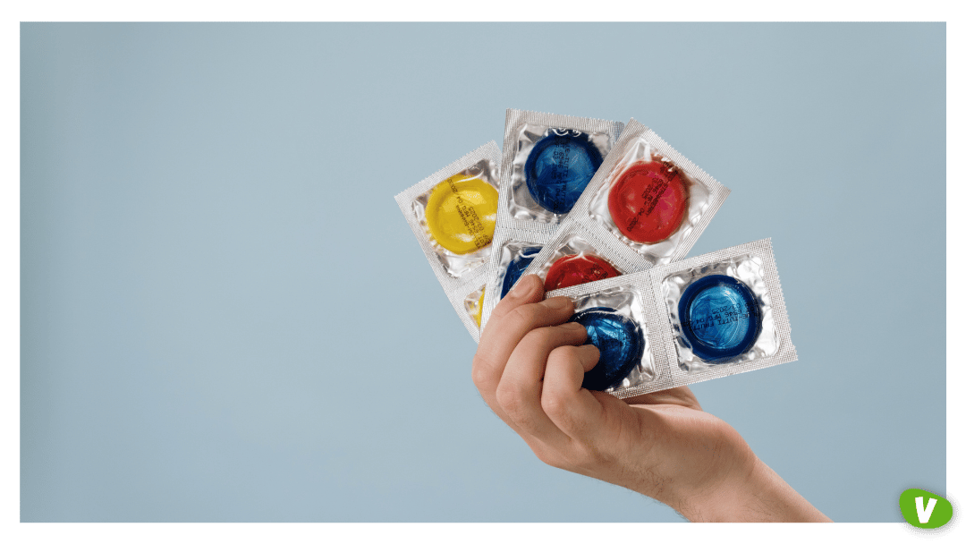 A hand holding several brightly coloured condoms in silver wrappers against a light blue background, highlighting safe and sustainable sex practices.