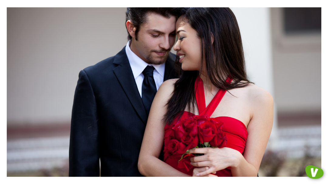 A man in a black suit and a woman in a red dress holding a bouquet of roses, sharing a tender moment that reflects the romance and companionship some seek with escorts.