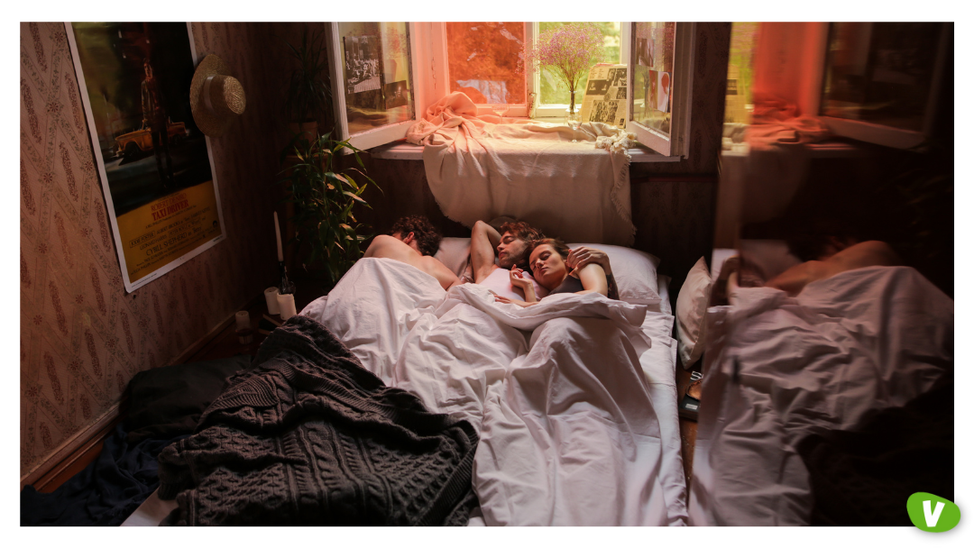 Three people lying together under white sheets in a cozy bedroom, representing a threesome with an escort, couple booking escort services, and how to arrange a three-way encounter respectfully.