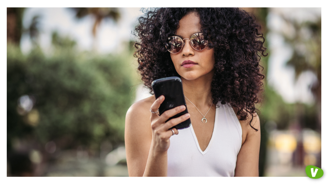 A young woman wearing sunglasses looking at her phone with a serious expression, illustrating how to spot timewasters in escorting, including screening escort clients and identifying sex work red flags.