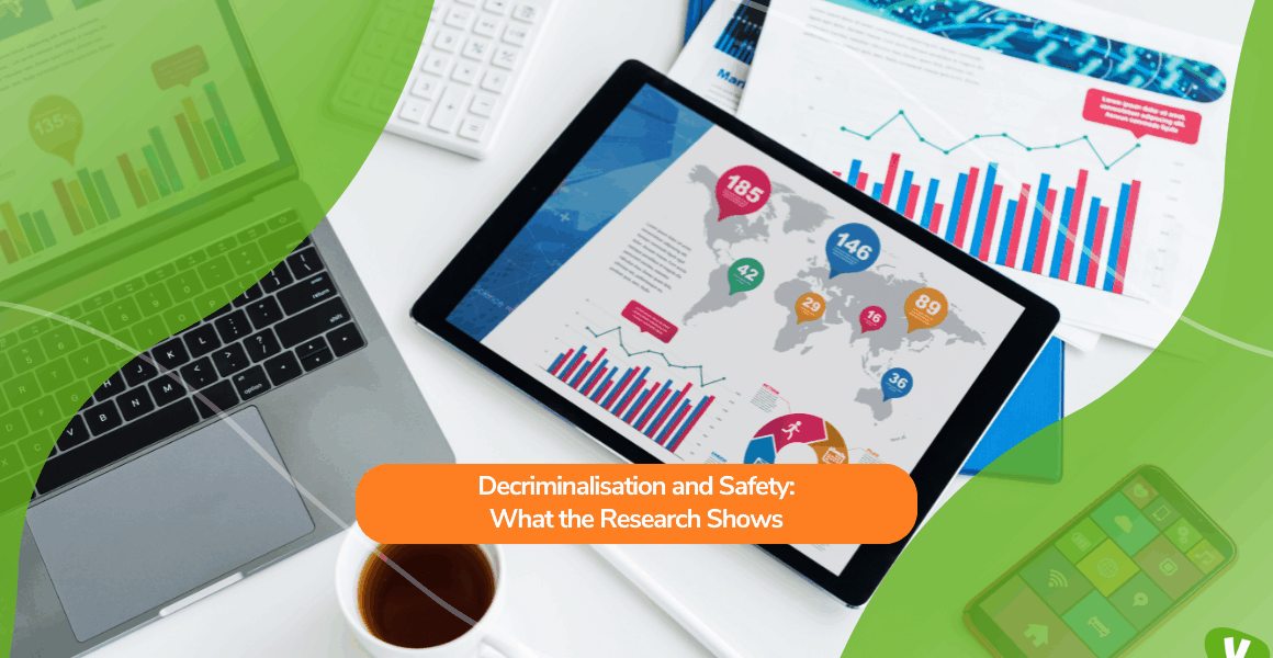 A workspace with a laptop, tablet, documents, and a cup of tea. The tablet displays colourful data charts and maps, representing research findings. Overlaid text reads: “Decriminalisation and Safety: What the Research Shows.”