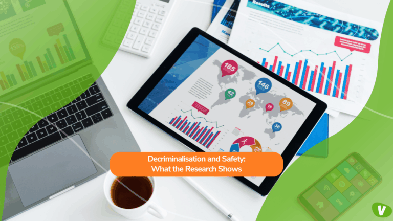 A workspace with a laptop, tablet, documents, and a cup of tea. The tablet displays colourful data charts and maps, representing research findings. Overlaid text reads: “Decriminalisation and Safety: What the Research Shows.”