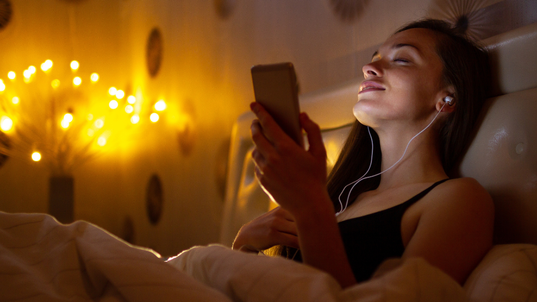 Woman in bed listening to voice notes from sext chat